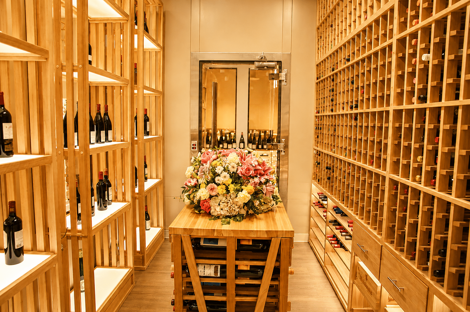 Interior of the Lotus of Siam wine room with wooden bottle racks, drawers, and a central table topped with flowers.